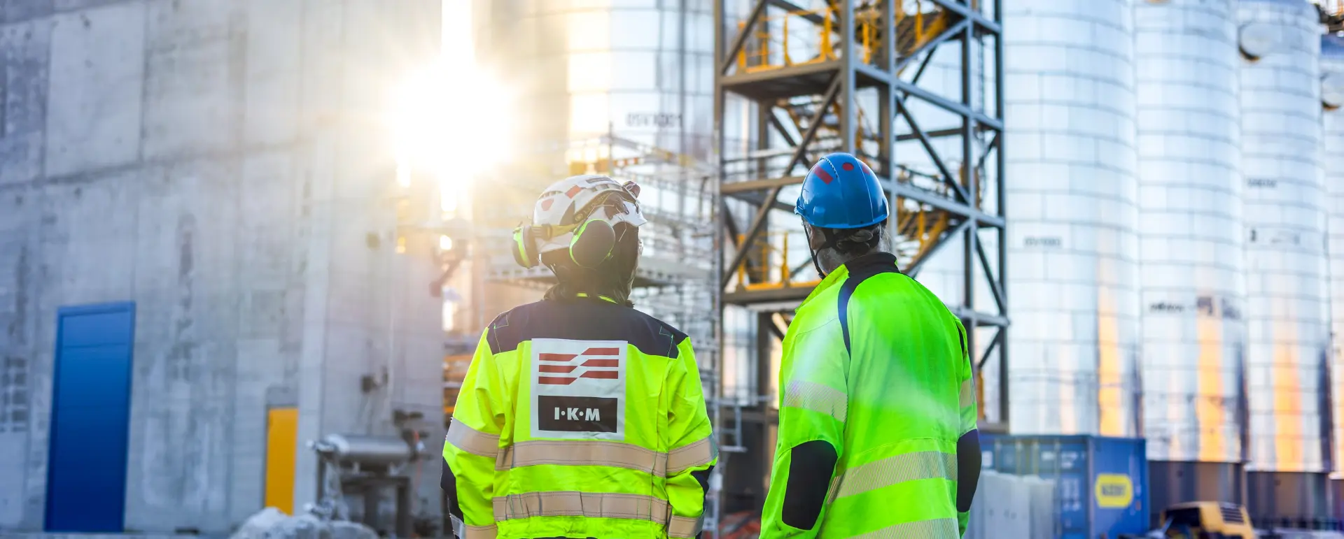 To arbeidere i verneutstyr som ser på industrimaskiner på en byggeplass.